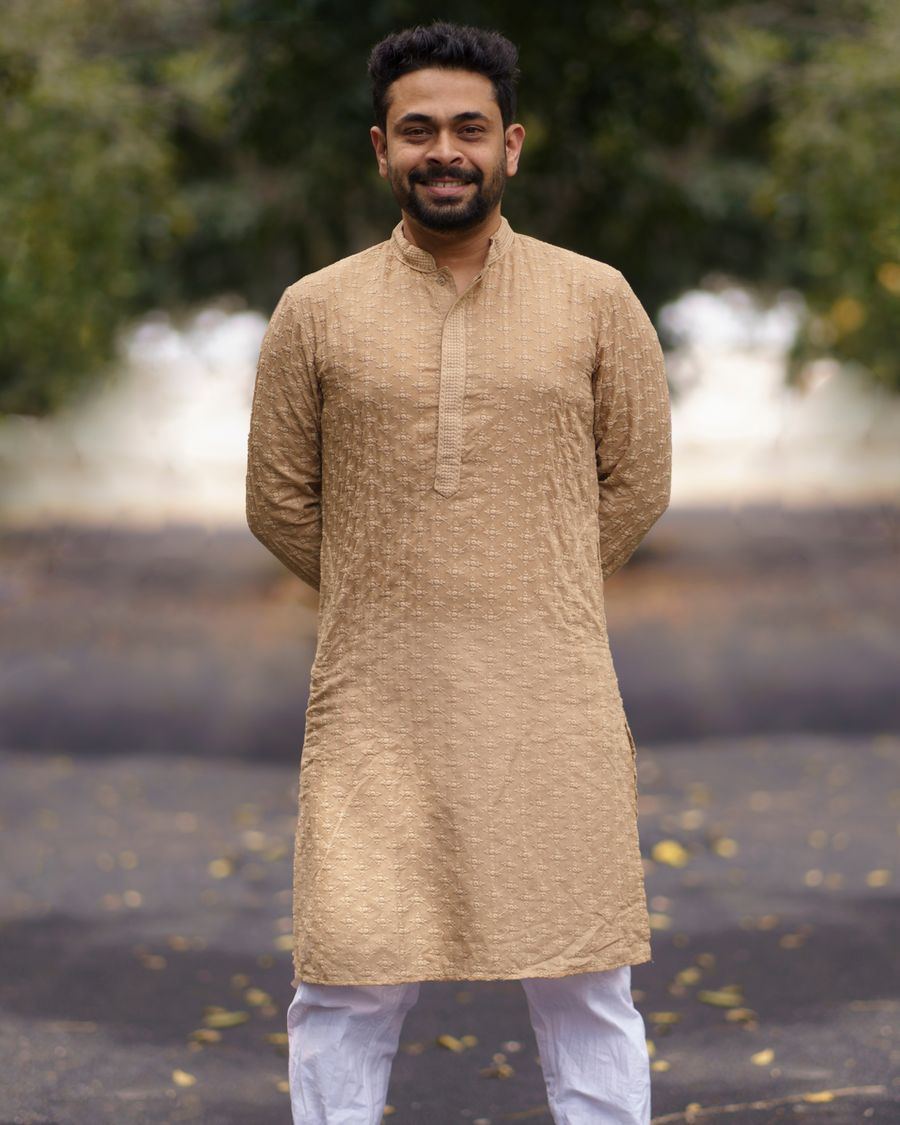 A smiling man in a sand-coloured embroidered kurta and white trousers